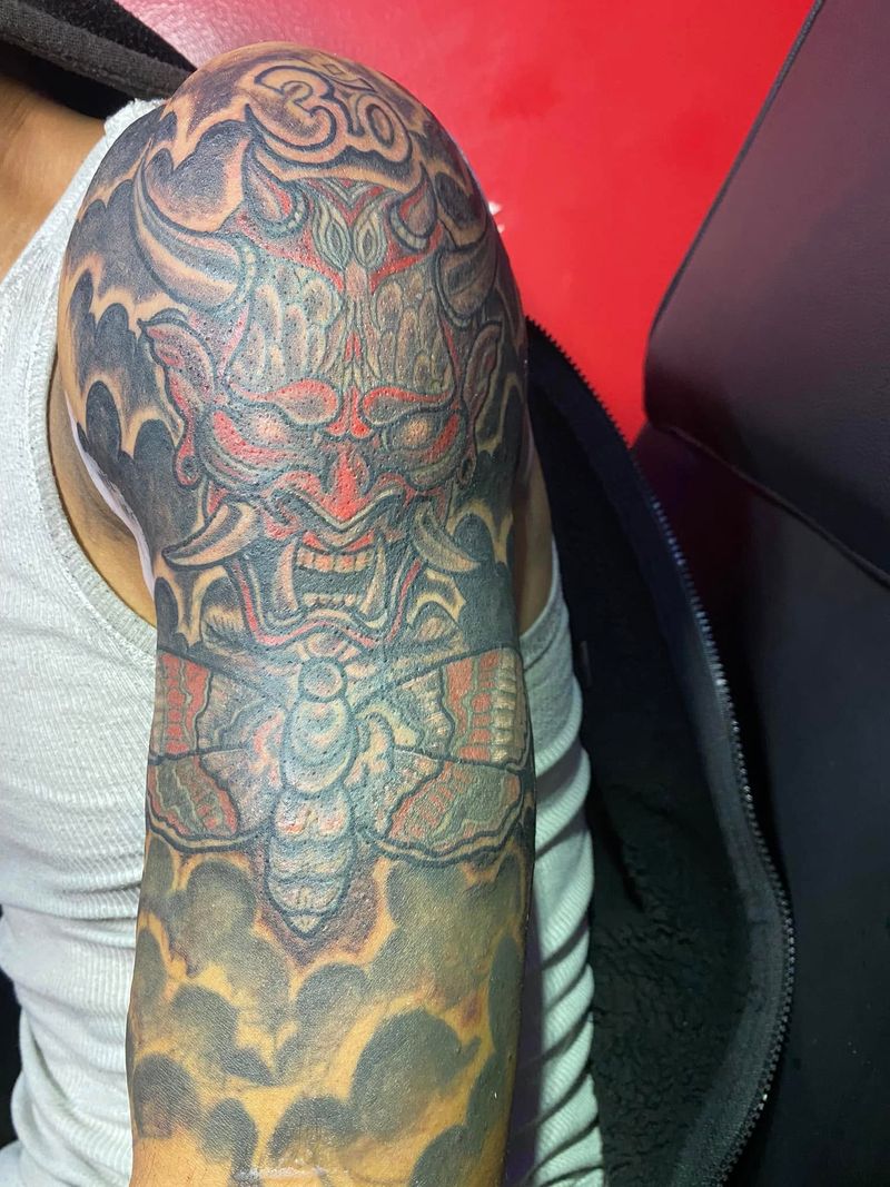 Color half sleeve tattoo of a red oni mask above a moth, surrounded by smoke and clouds, on a shoulder and upper arm.